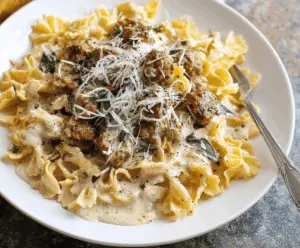 Creamy sausage Alfredo pasta dish topped with freshly grated Parmesan cheese and chopped parsley, served in a white bowl for a delicious comfort meal.