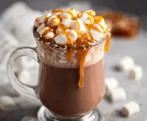 A steaming mug of salted caramel hot chocolate topped with whipped cream and a drizzle of caramel sauce.