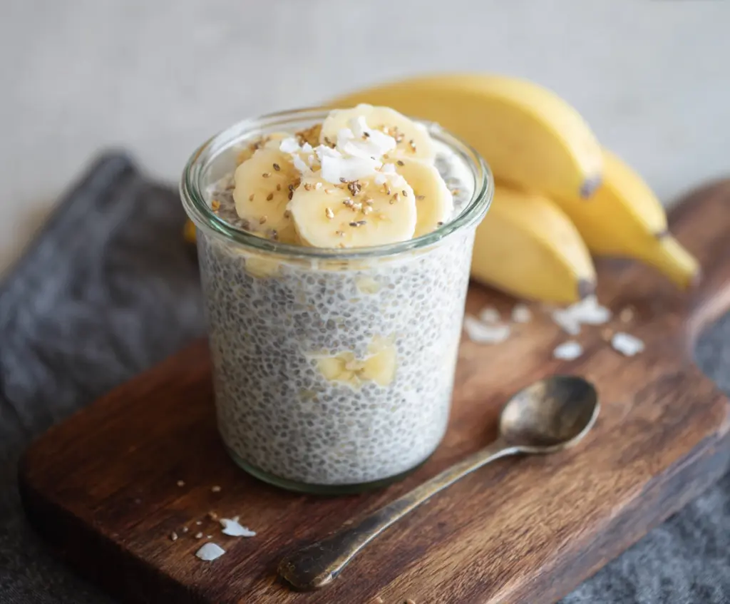 Creamy banana coconut milk chia seed pudding in a glass bowl, garnished with fresh banana slices and shredded coconut.