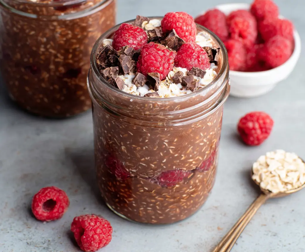 Creamy chocolate raspberry overnight oats served in a glass jar with fresh raspberries on top.