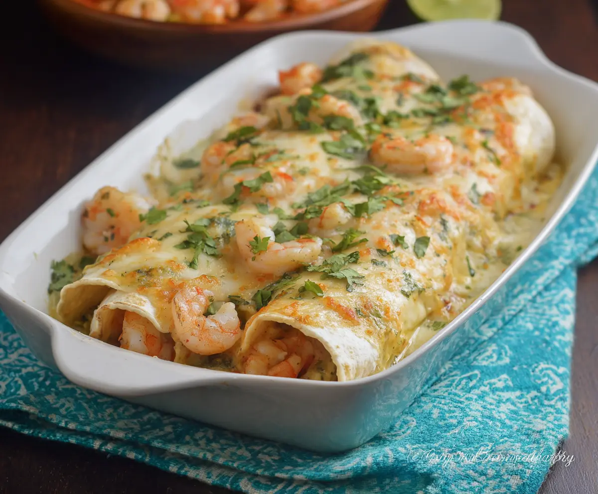 Delicious creamy shrimp enchiladas topped with cheese and fresh herbs on a white plate.