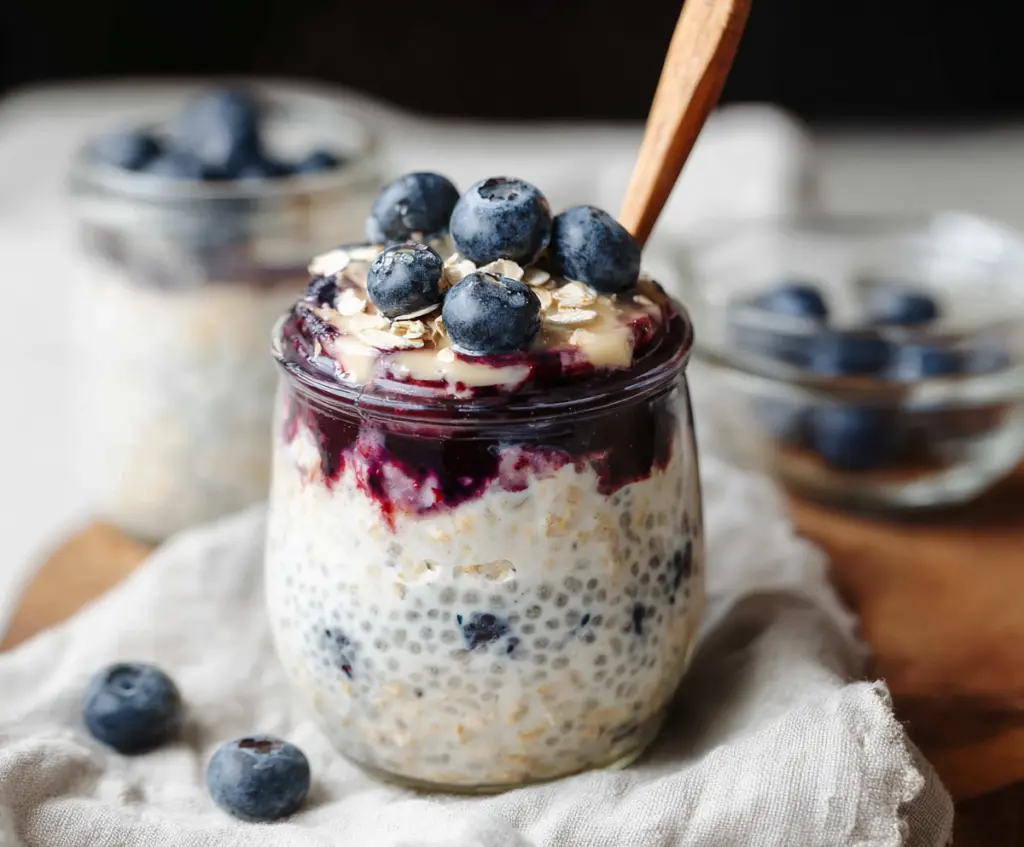 Creamy blueberry cheesecake overnight oats in a glass jar topped with fresh blueberries.