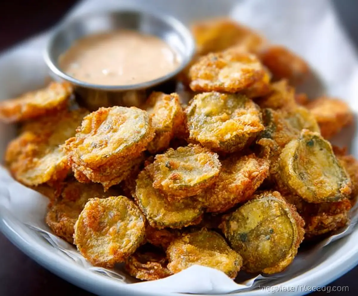 Crispy fried pickles served with a side of dipping sauce on a rustic plate.