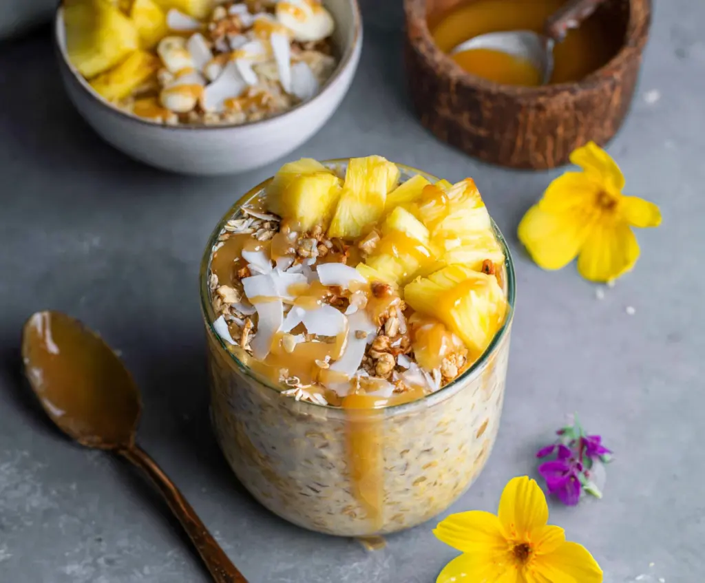 Creamy pineapple overnight oats in a glass jar topped with fresh pineapple pieces and chia seeds.