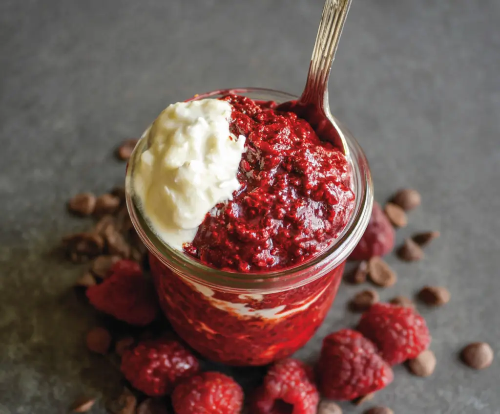Creamy red velvet overnight oats topped with whipped cream and chocolate shavings in a glass jar.