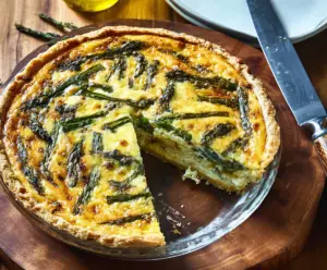Delicious asparagus and Gruyere cheese quiche on a rustic plate, perfect for brunch or lunch.