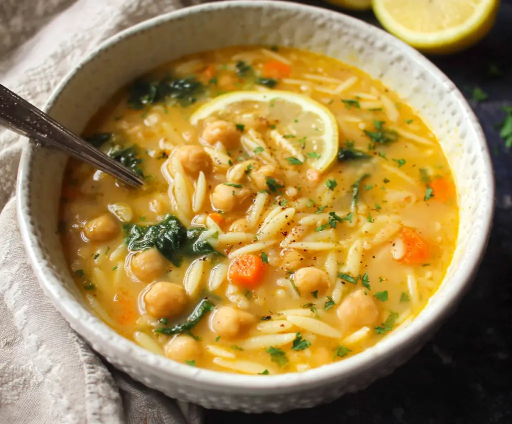 Creamy Lemon Chickpea Orzo Soup served in a white bowl, garnished with fresh herbs and lemon slices.