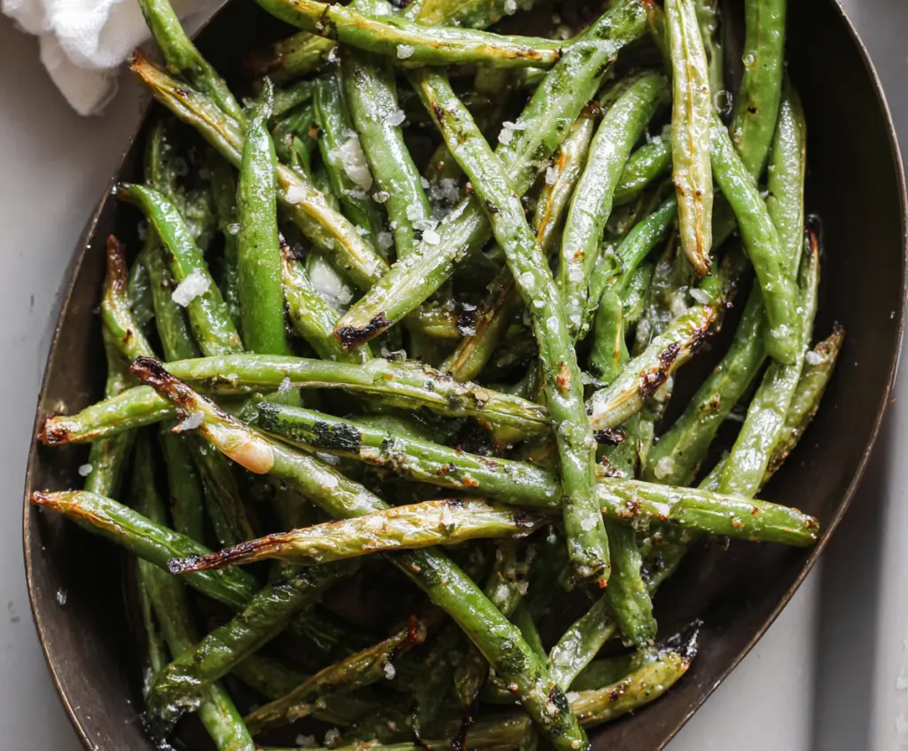 Delicious roasted green beans seasoned with herbs and spices on a white plate.